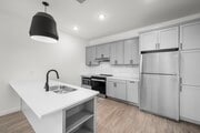 Cocina moderna con elegantes gabinetes grises, electrodomésticos de acero inoxidable y una elegante lámpara colgante sobre una espaciosa isla blanca.