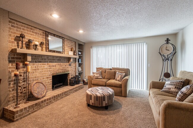 A cozy living room featuring a three-seater sofa, love seat, a fireplace, a floor clock, and a round coffee table, all bathed in warm lighting for the perfect, inviting space. - Wilshire Apartments