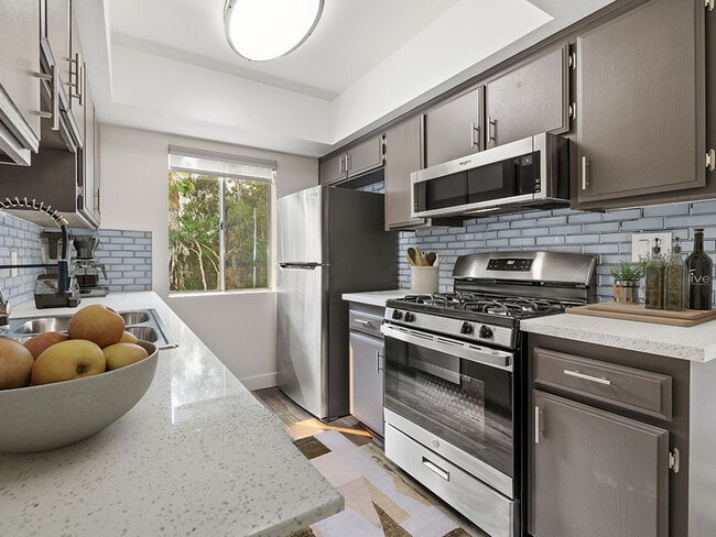 Tiled kitchen with stainless steel oven, microwave, and fridge. - Sherman Oaks Gardens Apartments