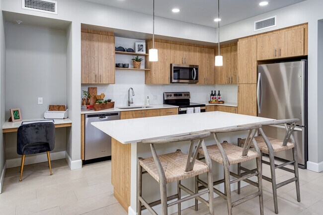 Open concept kitchen with quartz countertop, island, stainless steel appliances, tile backsplash and work from home nook