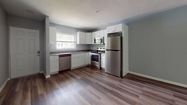 Modern kitchen with sleek stainless steel appliances, elegant white cabinetry, and warm wood flooring, offering an inviting and functional cooking space. - Sunny Creek Apartments