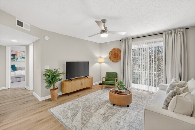 Spacious living room with ceiling fan and sliding glass door - Saddlebrook Apartments