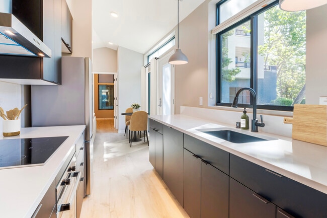 Freestanding home kitchen with stainless steel appliances, white quartz countertops, black cabinetry, and hard surface flooring