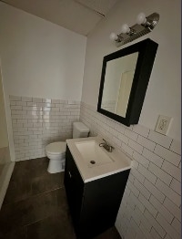 Cuenta con azulejos blancos clásicos tipo metro, pisos de baldosas y un tocador moderno, creando un ambiente limpio y atemporal. - 353 High St