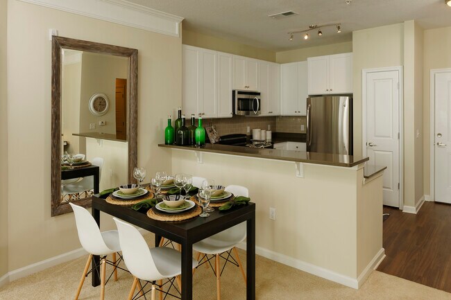 Dining area and kitchen with quartz stone countertop, white cabinetry, tile backsplash, stainless steel appliances and hard surface flooring