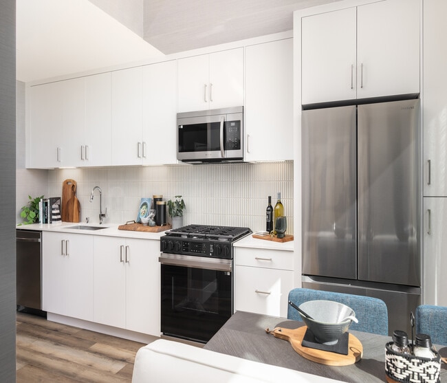Bright, modern kitchen with sleek stainless steel appliances, abundant white cabinetry, and stylish wood flooring. Perfect for culinary creativity.