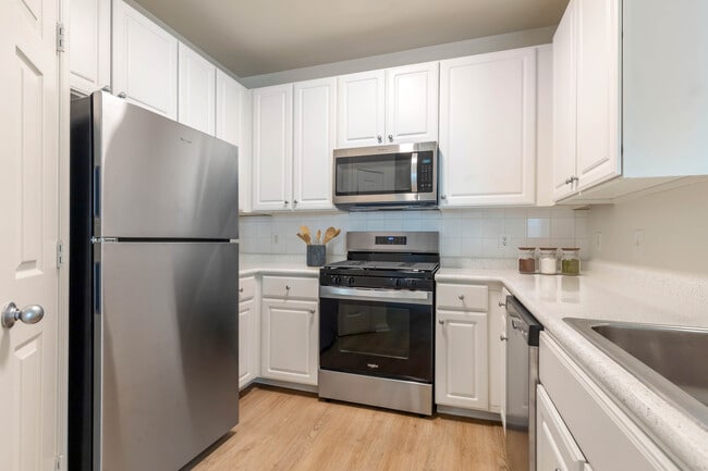 Cocina clásica I con gabinetes blancos, encimeras laminadas blancas, placa para salpicaduras de azulejos blancos, electrodomésticos de acero inoxidable y pisos de superficie dura.