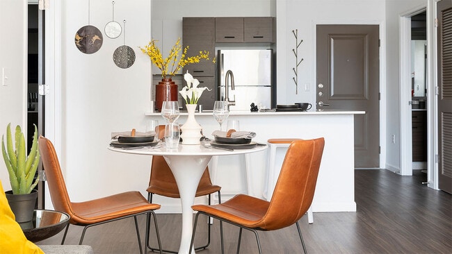 Apartment kitchen with stainless steel appliances and dining room with wood-style flooring.