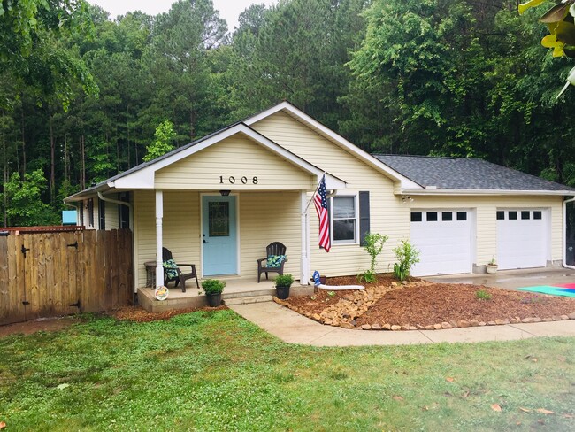 Full front view of the home with the large two car garage, recent landscaping of the front beds, and a view to the back yard beyond the fence. Tree surround provides a peaceful retreat. - 1008 Carpenter Fletcher Rd Casa