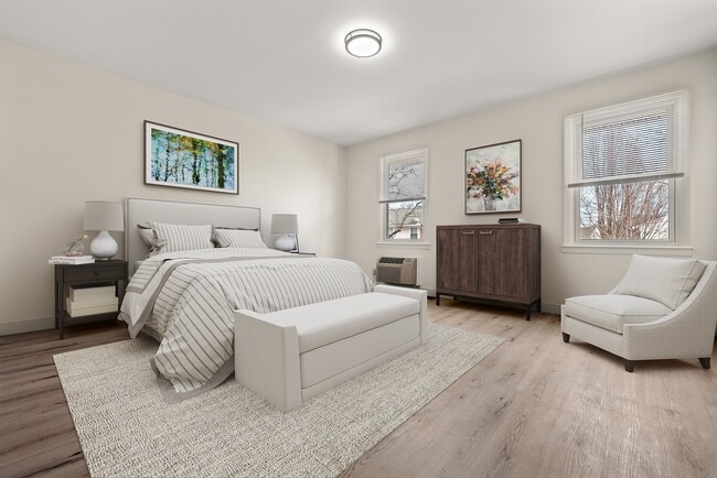 Bright and elegant bedroom featuring a cozy bed with striped linens, modern furnishings, and large windows with natural light. - Stony Brook Commons