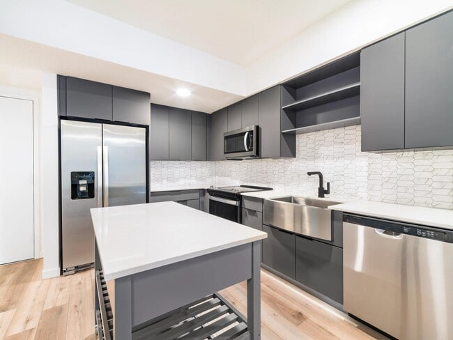 Premium finish kitchen with charcoal cabinetry, quartz countertops, a workstation sink, matte black fixtures, and stainless steel appliances.