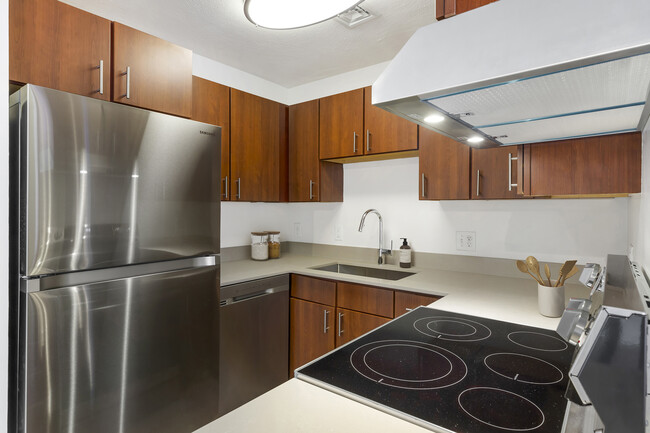 Renovated Package III kitchen with stainless steel appliances, grey quartz countertops, white or cherry cabinetry, and hard surface flooring - eaves Quincy Apartments