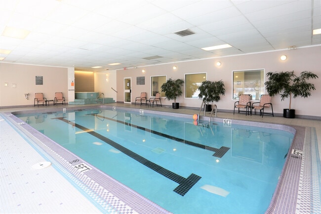 Elegant indoor swimming pool area with comfortable seating and lush greenery, perfect for relaxation and leisure. - Village in the Park Apartments