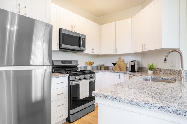 Renovated Package I kitchen with white cabinetry, grey granite countertops, stainless steel appliances, and hard surface plank flooring - Avalon Russett Apartments