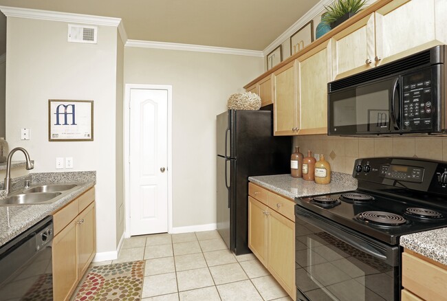 Kitchen with oak cabinetry, speckled granite countertops, black appliances, and hard surface flooring - eaves Twin Creeks Apartments