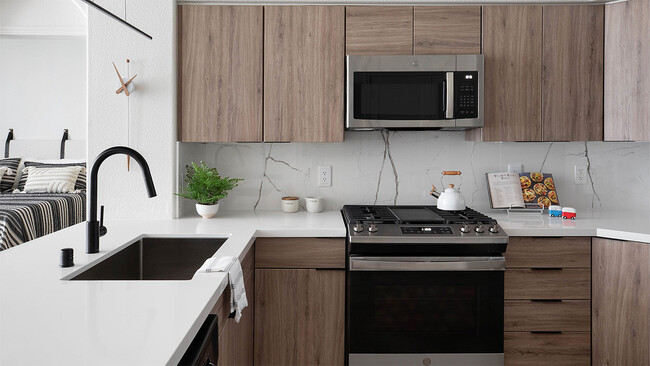 Apartment kitchen with stainless steel appliances, quartz countertops, and wood-style flooring. - Griffis Mission Valley Rental