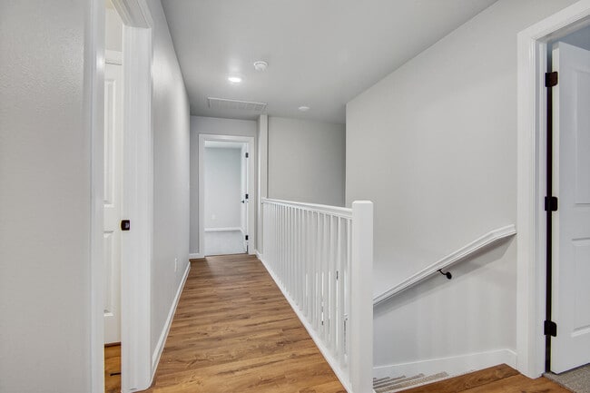 Upstairs hallway with wood style flooring, white railing, recessed lighting, and doorways leading to bedrooms