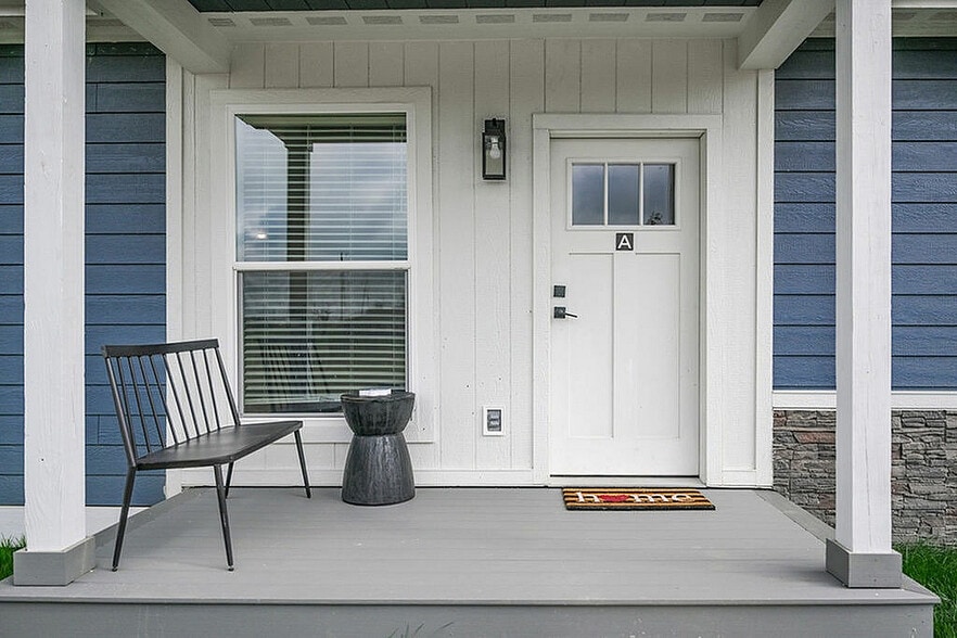 Inviting porch of a charming home featuring a white front door with a welcoming doormat, complemented by a stylish black bench and a modern side table.