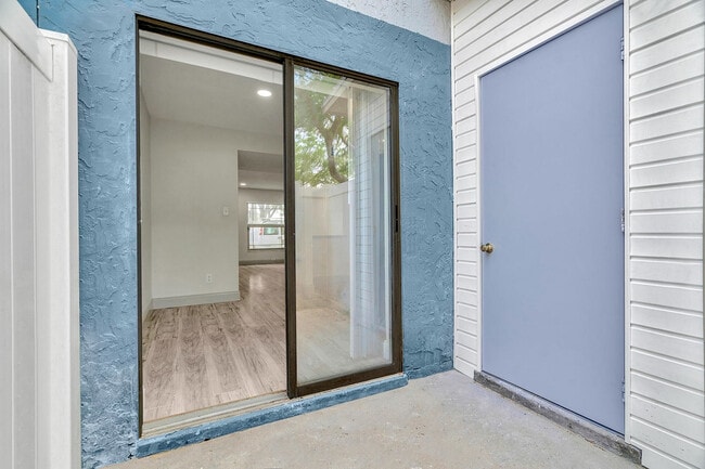 Inviting apartment entrance with modern sliding glass door opening to bright, spacious interior featuring elegant wood flooring.
