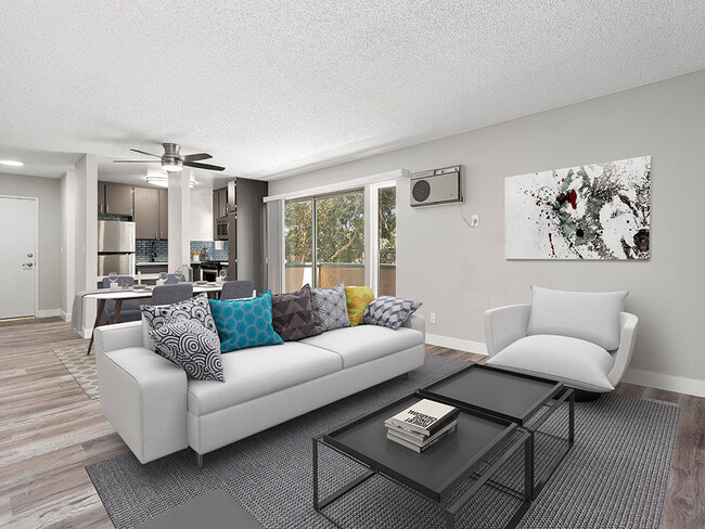 Hardwood floored living room with view of dining area, kitchen, and balcony. - Olive View Gardens Apartments