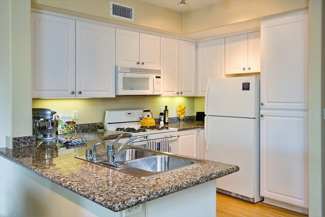 Classic Package I kitchen with white appliances, beige speckled granite countertop, white cabinetry, and hard surface flooring