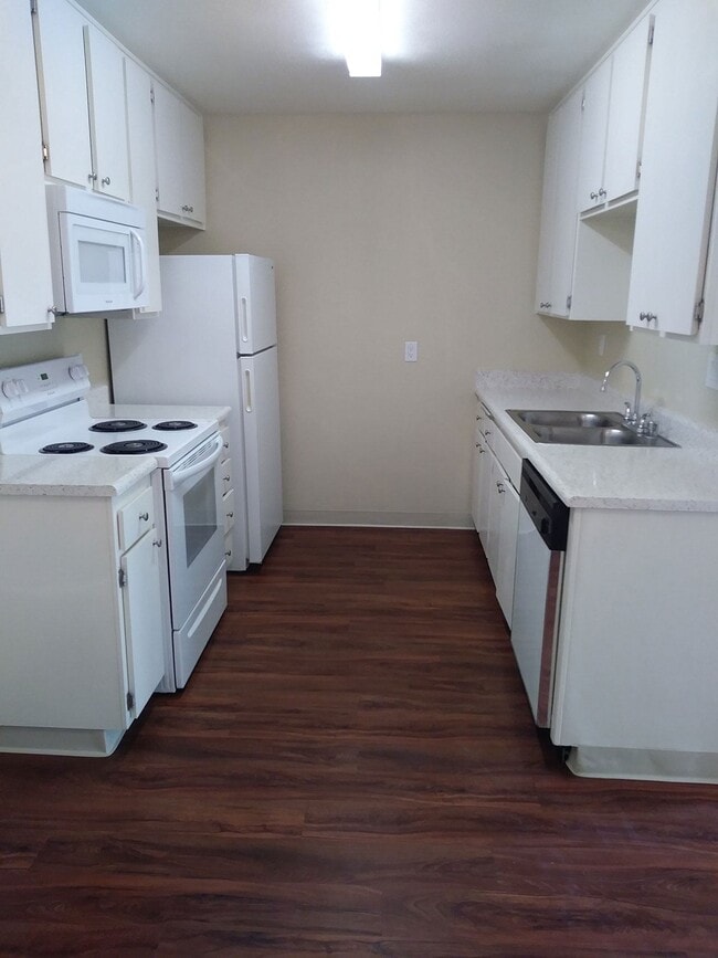 Kitchen with dark hardwood flooring and white kitchen appliances and cabinets at Teton Pines Apartments in Escondido, California.