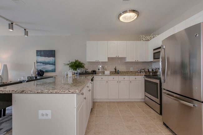 Open concept kitchen with white cabinetry, cream tile backsplash, stainless-steel appliances, granite countertops and hard surface flooring
