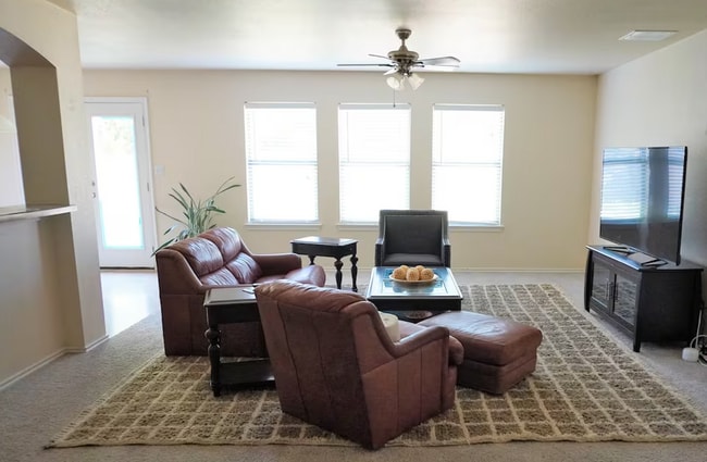 Living room comes with ceiling fan, comfortable sofas, coffee table, and 65" TV - 15106 Parrish Ln