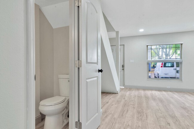 Modern apartment interior featuring sleek hardwood flooring, fresh white paint, and a bright, inviting space with a convenient half-bathroom.