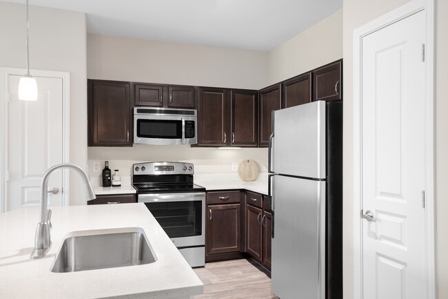 Kitchen with stainless steel appliances, quartz or granite countertops, espresso cabinetry, and hard surface vinyl plank flooring - Avalon at Pier 121 Apartments