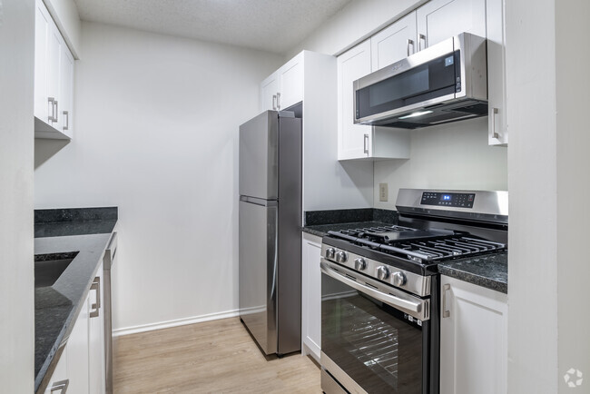 Renovated Package II kitchen with stainless steel appliances, granite countertops, white cabinetry, and hard surface flooring - eaves Fair Lakes Rental