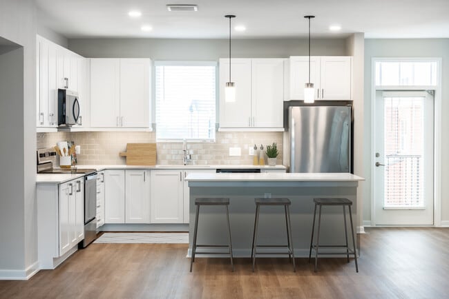 Finish Package I townhome kitchen with stainless steel appliances, white cabinetry, grey tile backsplash, white quartz countertops, and hard surface flooring