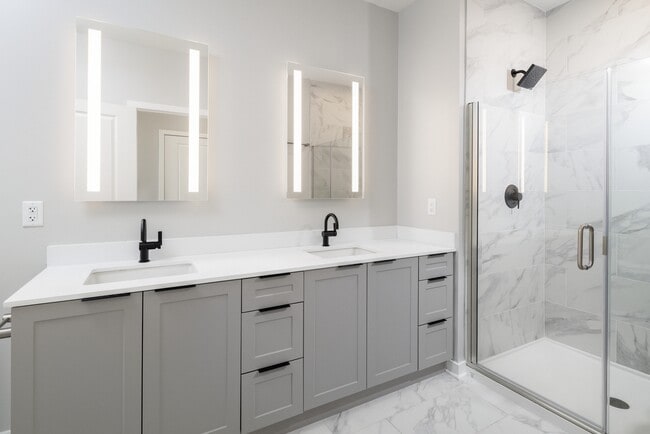 Signature Collection bath with dual vanity sinks, grey shaker cabinetry, white quartz countertop, and LED vanity mirrors