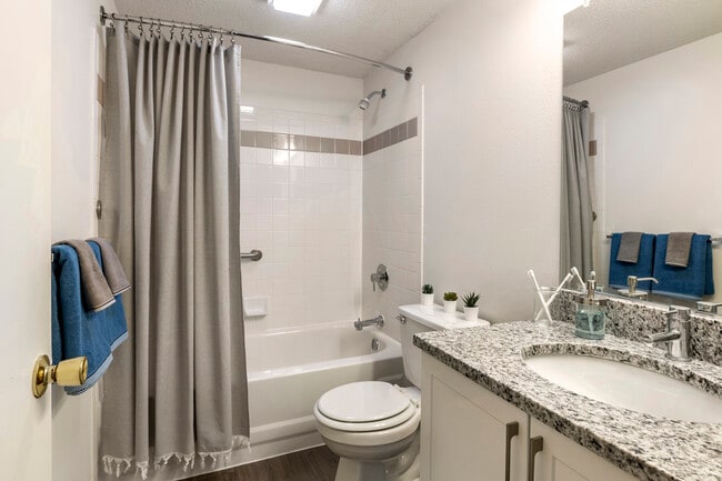 Renovated Package III bath with white cabinetry, grey granite countertops, and shower and bath with tile backsplash