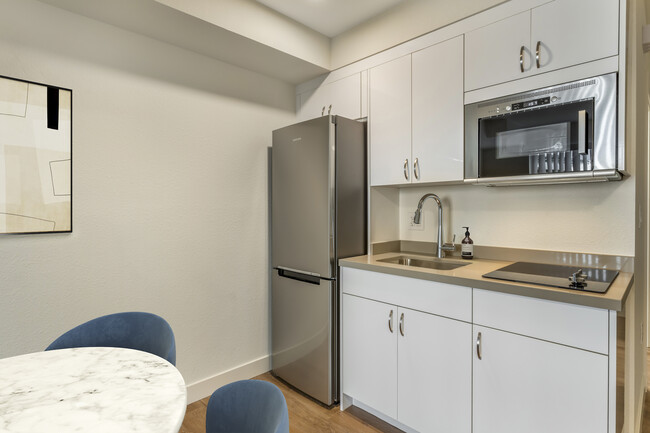 Renovated Package II kitchen with stainless steel appliances, beige quartz countertops, white cabinetry, and hard surface flooring - eaves Mountain View at Middlefield Apartments