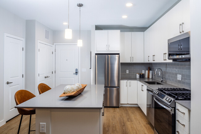 Modern kitchen with white cabinetry, grey tile backsplash, grey quartz countertops, and stainless steel appliances - Avalon North Andover Apartments