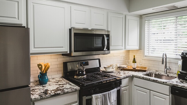 Un moderno placa para salpicaduras de azulejos blancos y gabinetes de color blanco de búsqueda de coincidencias adornan nuestros apartamentos renovados