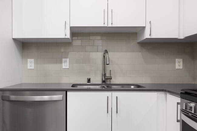 Renovated Package I kitchen with quartz countertops, white cabinetry, stainless steel appliances, hard surface vinyl plank flooring, and tile backsplash - Avalon Playa Vista