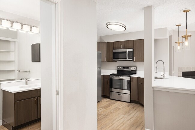 Modern apartment kitchen with elegant white countertops, stainless steel appliances, and warm wood flooring.