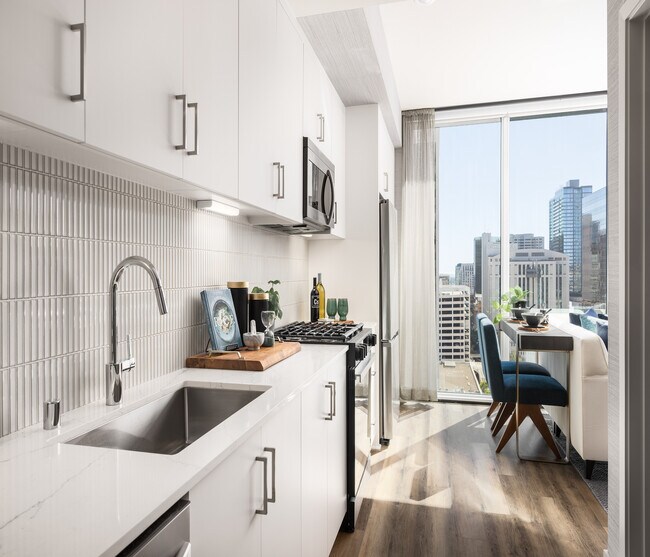 Modern kitchen with sleek white cabinets, stainless steel appliances, and a stunning city view, perfect for urban living.