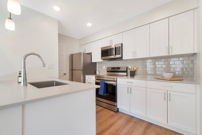 Renovated Package II kitchen with stainless steel appliances, beige quartz countertops, white cabinetry, light grey tile backsplash, and hard surface flooring - eaves West Windsor