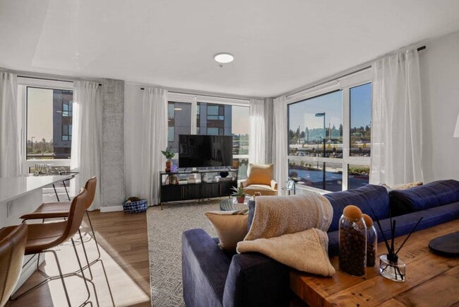 Modelo de 2 dormitorios: sala de estar con grandes ventanales y techos altos. - Riverfront Everett
