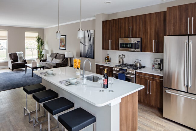 Townhome Signature Collection Kitchen with oak cabinetry, light grey quartz countertops, white tile backsplash, and hard surface flooring. Upgraded stainless steel appliances with French door refrigerator.