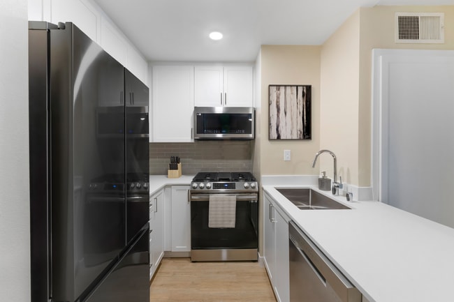 Renovated Package I kitchen with stainless steel appliances, white quartz countertops, white cabinetry, grey tile backsplash, and hard surface flooring - Avalon Burbank Apartments