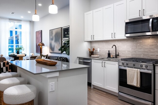 Upgrade Collection kitchen with white shaker cabinetry, grey quartz countertops, beige tile backsplash, and stainless steel appliances