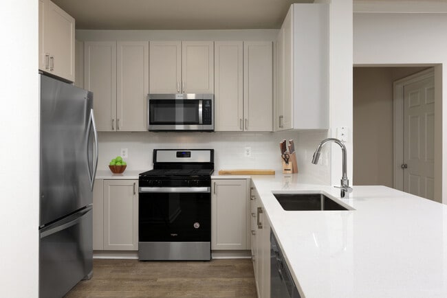 Renovado II cocina con gabinetes de color gris, encimeras de cuarzo blancas, electrodomésticos de acero inoxidable, placa para salpicaduras de azulejos blancos, y pisos de superficie dura