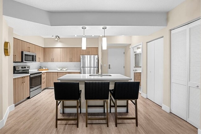 Modern kitchens include USB charging ports, islands, pendant lighting, wood-grain cabinets and stainless steel appliances - The District Boynton