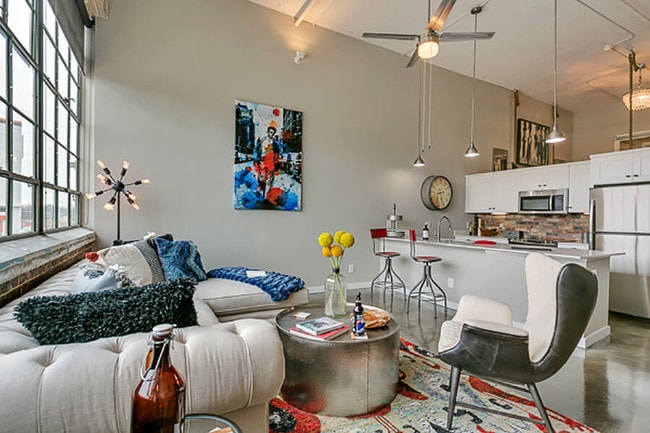 Living room with open concept kitchen, concrete floor, and beautiful white cabinets. Loft style apartment - Lofts at Mockingbird Station Apartments