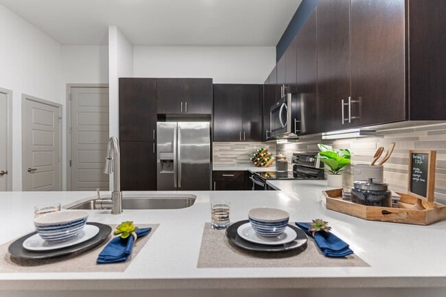 Our contemporary kitchens feature under-cabinet lighting and premium quartz countertops with tile backsplash - Stella Apartments