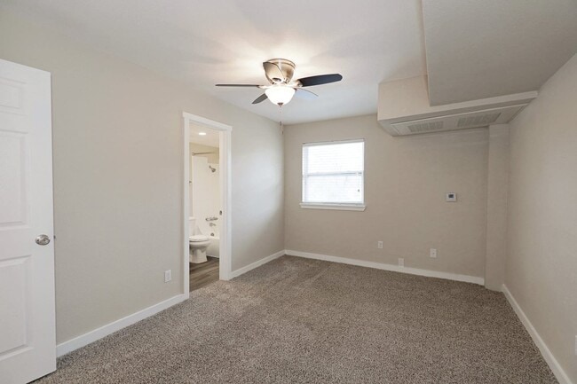 Bedroom with carpet flooring, ceiling fan, window with blinds, and doorway leading to bathroom and adjacent room
